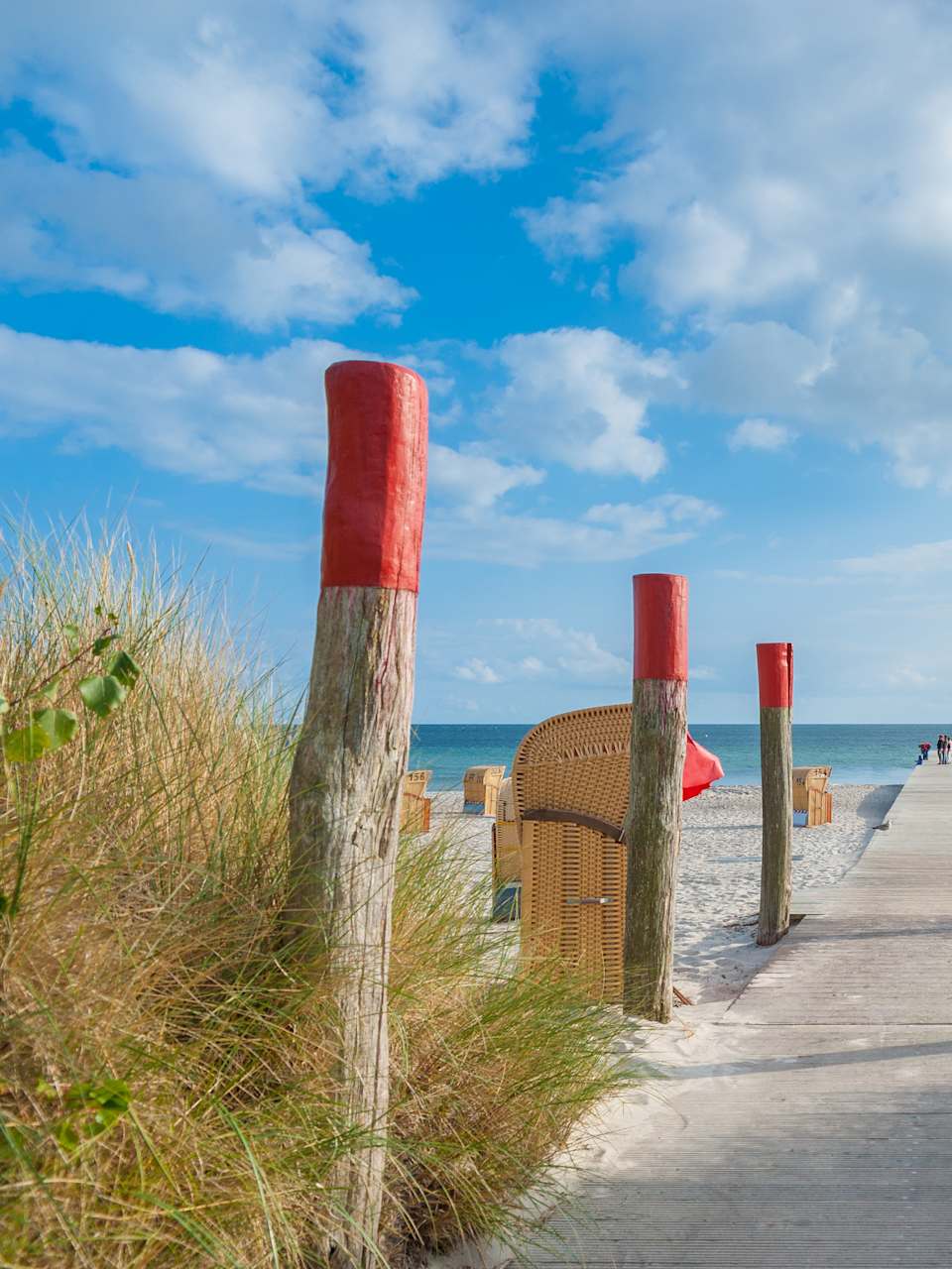 Ein Holzsteg führt zum Meer an einem Strand mit Strandkörben